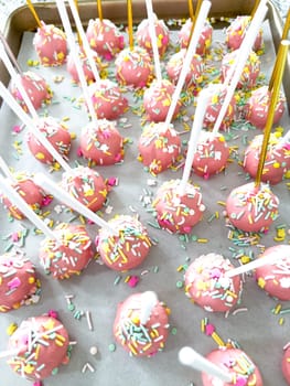 Arrayed neatly on parchment, these hand-dipped pink cake pops are a playful treat, adorned with a rainbow of sprinkles that add a festive touch to the sweet delights.