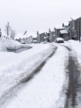 Castle Rock, Colorado, USA-March 16, 2024-Fresh tire tracks curve along a snow-covered street, carving a path through the freshly fallen flakes piled high on either side.