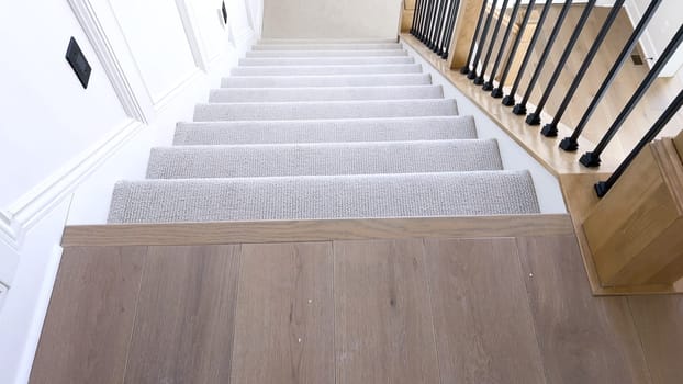 The image captures the detail of a well-designed modern staircase, lined with plush beige carpet, complemented by white walls and wooden balusters.