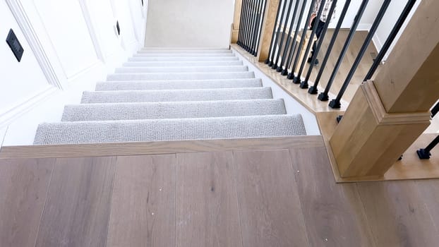 The image captures the detail of a well-designed modern staircase, lined with plush beige carpet, complemented by white walls and wooden balusters.