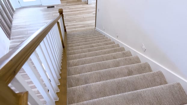 The image captures the detail of a well-designed modern staircase, lined with plush beige carpet, complemented by white walls and wooden balusters.