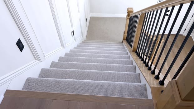 The image captures the detail of a well-designed modern staircase, lined with plush beige carpet, complemented by white walls and wooden balusters.