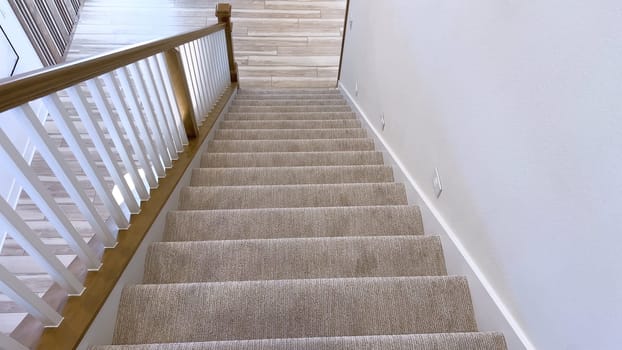 The image captures the detail of a well-designed modern staircase, lined with plush beige carpet, complemented by white walls and wooden balusters.