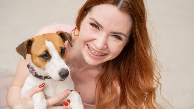 Dog jack russell terrier licks the owner in the face outdoors. Girl with braces on her teeth