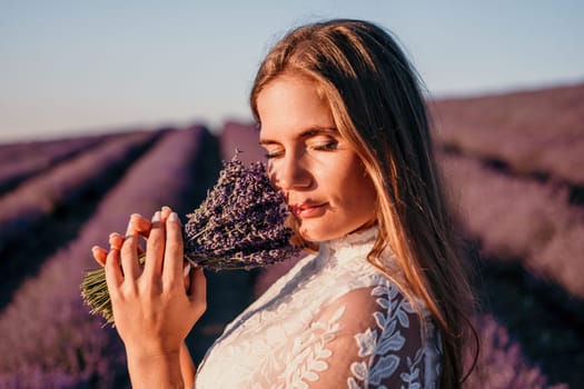 Close up portrait of young beautiful woman in a white dress and a hat is walking in the lavender field and smelling lavender bouquet.