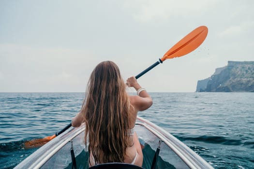 Woman in kayak back view. Happy young woman with long hair floating in transparent kayak on the crystal clear sea. Summer holiday vacation and cheerful female people having fun on the boat.