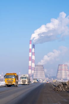 Naberezhnye Chelny, Russia, March 2, 2024. A factory with smoke billowing from its chimneys against the cloudy sky, as vehicles pass by on the asphalt road, reflecting in automotive sideview mirrors