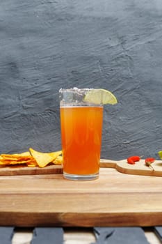 Michelada cocktail with tomato juice, beer and lime in a glass and nachos. Vertical photo