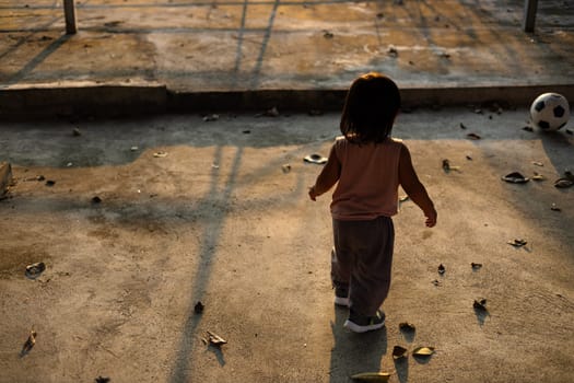 Asian boy plays football on the cement ground. boy plays in the outdoor taken from the back side.