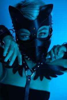 portrait of a hot sexy girl in a leather cat mask and muzzled in bdsm handcuffs on neon blue light background