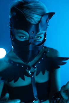 portrait of a hot sexy girl in a leather cat mask and muzzled in bdsm handcuffs on neon blue light background