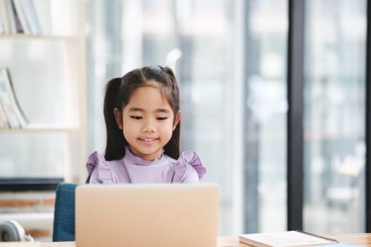 A young girl is sitting at a desk with a laptop in front of her. She is smiling and she is enjoying her time. The room is filled with books