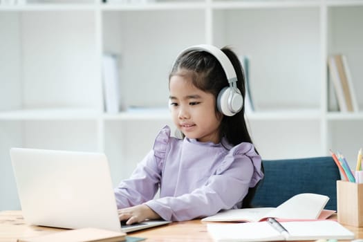 A young girl is sitting at a desk with a laptop and headphones on. She is smiling and she is enjoying her work. The scene suggests that she is engaged in an educational or creative activity
