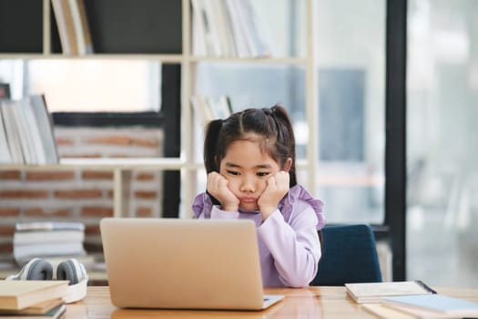 A young student appears disinterested and bored while engaging with an online class on her laptop.