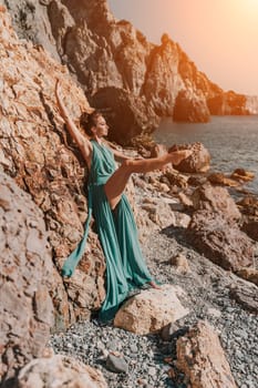 Woman green dress sea. Woman in a long mint dress posing on a beach with rocks on sunny day. Girl on the nature on blue sky background