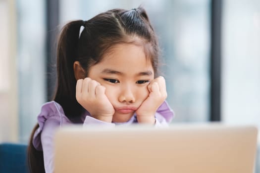 A young student appears disinterested and bored while engaging with an online class on her laptop.