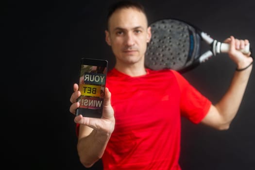 man holding paddel racket and smartphone with sports betting on black background. High quality photo