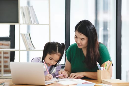 A woman is helping a young girl with her homework. The girl is using a laptop to complete her assignment. The woman is sitting next to her, providing guidance and support