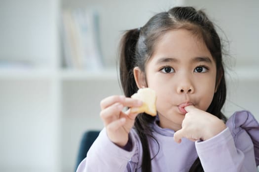 A young girl is eating a piece of fruit. She is wearing a purple shirt and has her hair in pigtails