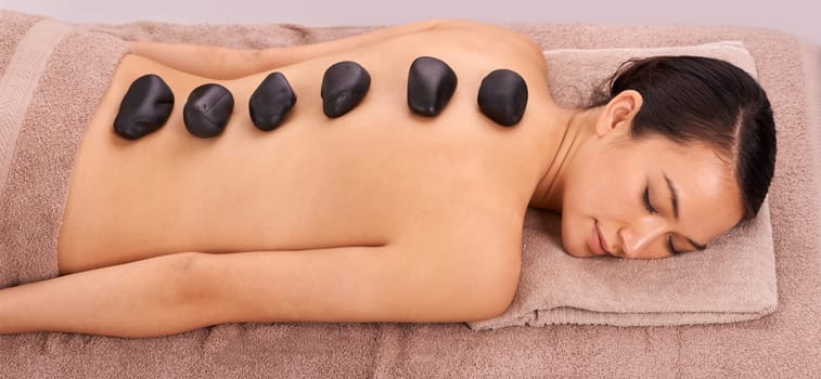 Calm, hot stone and woman with back massage at spa for wellness, self care and grooming treatment for healing. Skin, girl and high angle of person with warm rock body routine on table for zen