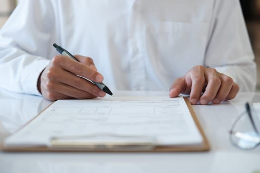 A man is writing on a piece of paper with a pen. He is wearing a white shirt and he is focused on his writing. Concept of concentration and determination as the man puts pen to paper