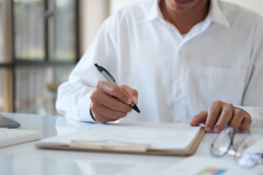 A man is writing on a piece of paper with a pen. He is wearing a white shirt and glasses