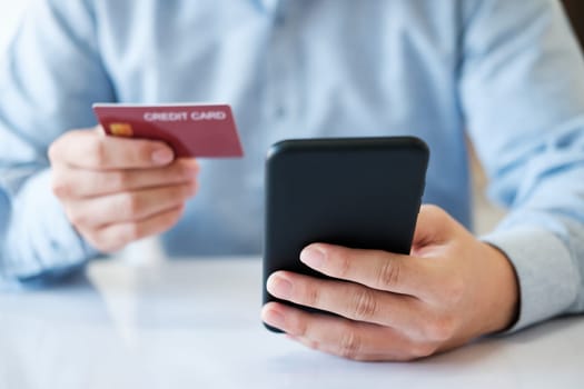 A man is using his phone to pay for a credit card. He is holding the credit card in one hand and the phone in the other