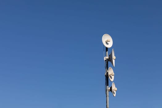 White telecommunications antennas on a single mast high above the city against the background of a blue sky. Technology of digital sending and receiving of data packets.