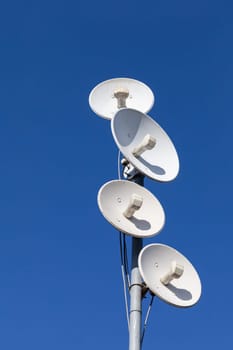 White telecommunications antennas on a single mast high above the city against the background of a blue sky. Technology of digital sending and receiving of data packets.