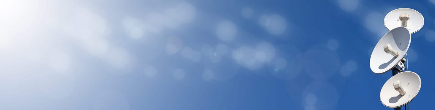 White telecommunications antennas on a single mast high above the city against the background of a blue sky. Technology of digital sending and receiving of data packets. Panoramic view. Blue background.