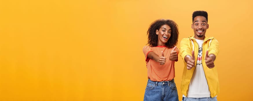 Two friends like perfect and awesome plan. Portrait of joyful friendly-looking optimistic african american female and male showing thumbs up in approval and agreement gesture smiling broadly. Copy space