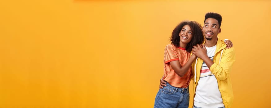 Couple of lovers enjoying spending warm summer evening together gazing up at stars with happy. enthusiastic expression being in love hugging and expressing warm romantic feelings over orange wall.