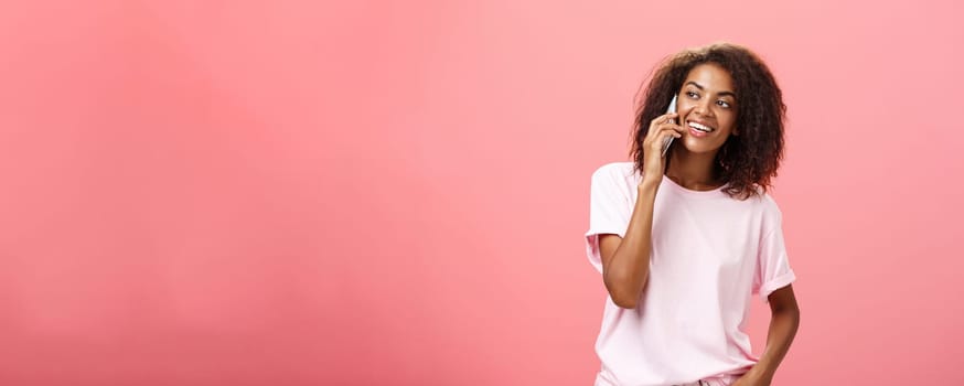 Girl calling friend to meet up. Portrait of charming friendly and outgoing african american young woman with afro hairstyle holding smartphone near ear while talking looking left curiously. Copy space