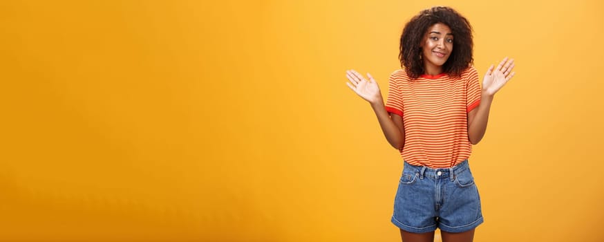 No idea do not care. Careless and indifferent calm happy african american woman with curly hair in summer clothes raising palms and shrugging in uninvolved pose smiling carefree being unaware. Body language concept