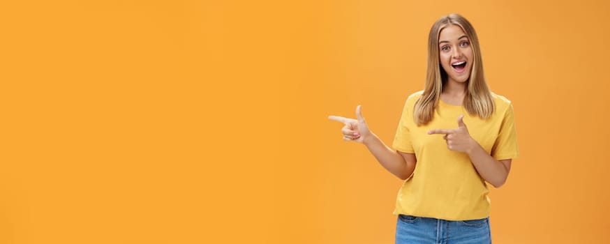 Check out copy sapce of dream. Upbeat good-looking pleasant female shop assistant in t-shirt pointing left with finger guns and smiling amused at camera recommending to watch that direction. Advertisement concept