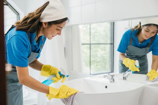 Focused on chores a woman in uniform cleans bathroom sink and faucet with spray. Her dedication to housework ensures purity hygiene and shiny fixtures. spray cleaner