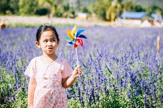 Portrait of a smiling girl in a flower garden holding a toy pinwheel. Spring brings joy and the spinning pinwheel signifies childhood fun freedom and happiness in nature's bright and sunny ambiance.