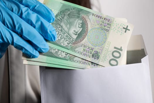 The woman slips a bundle of one hundred Polish zloty banknotes into a white envelope.
