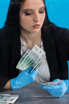 Hand counting banknotes by a young woman at the cashier's window in a large banking branch.
