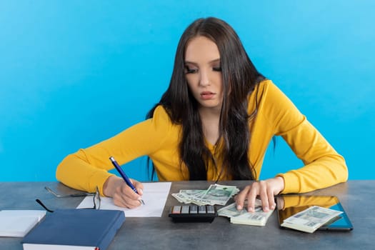 While counting money, a young woman uses a calculator and a tablet to check the stock exchange.