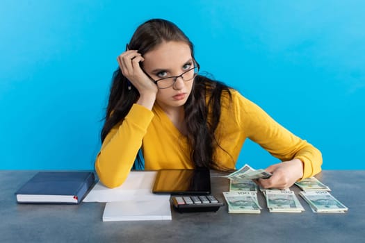 While counting money, a young woman uses a calculator and a tablet to check the stock exchange.