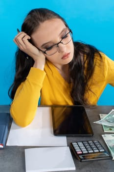 While counting money, a young woman uses a calculator and a tablet to check the stock exchange.