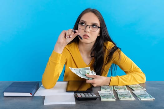 While counting money, a young woman uses a calculator and a tablet to check the stock exchange.