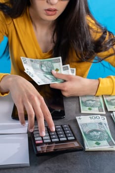 While counting money, a young woman uses a calculator and a tablet to check the stock exchange.