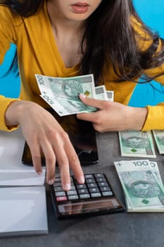 While counting money, a young woman uses a calculator and a tablet to check the stock exchange.