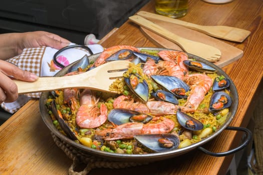 A person serving seafood paella with a wooden spatula from a traditional pan, typical Spanish cuisine, Majorca, Balearic Islands, Spain,