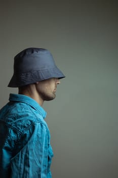 A stylish young male model with a well-groomed beard wearing a blue shirt and a dark hat, confidently posing for the camera.