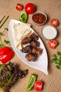 liver kebab with pita bread on a white plate with vegetables and herbs.