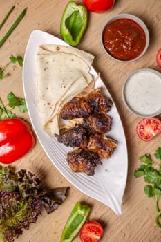 liver kebab with pita bread on a white plate with vegetables and herbs.