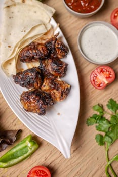 liver kebab with pita bread on a white plate with vegetables and herbs.